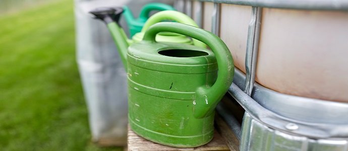 farming, gardening and agriculture concept - watering cans at farm water tank